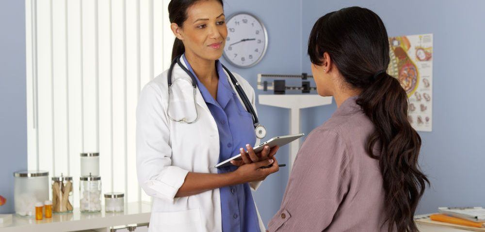 Ärztin in weißem Kittel empfängt eine junge Frau in ihrer Praxis zu einem Arztbesuch während der Arbeitszeit