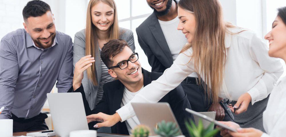 Erfolgreich sein in der VUCA Welt: Ein Team aus drei Männern und drei Frauen sitzt um einen Laptop herum und diskutiert angeregt