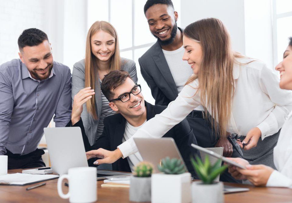 Erfolgreich sein in der VUCA Welt: Ein Team aus drei Männern und drei Frauen sitzt um einen Laptop herum und diskutiert angeregt