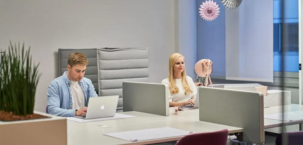 Ein junger Mann und eine junge Frau sitzen nebeneinander in einem Coworking Space und arbeiten an ihren Laptops.